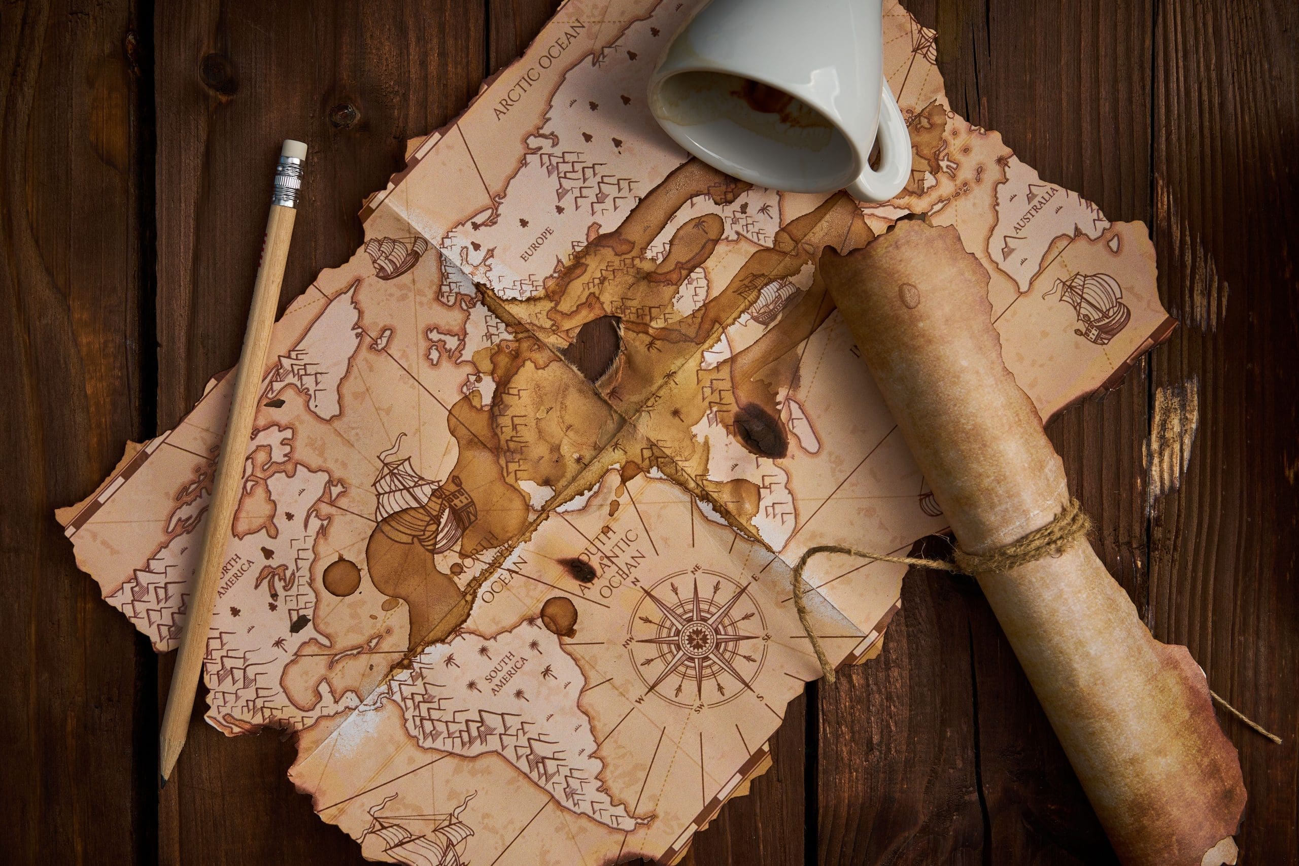 Aged parchment scroll, an old map, a pencil, and a spilled coffee cup on a wooden table. اختيار الحبوب المناسبة لذوقك